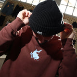 Person wearing a black beanie and maroon hoodie with a logo, indoors.