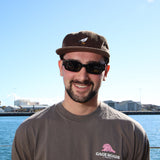 Man wearing sunglasses and a cap with a logo on a waterfront background